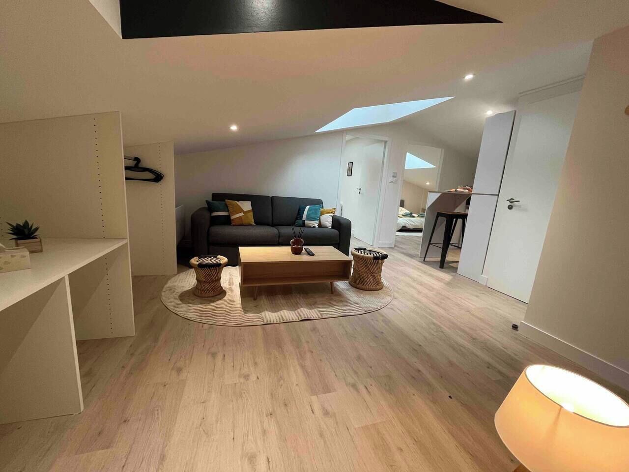 Een moderne woonkamer met een bank, salontafel en twee bijzettafeltjes. Boven de bank bevindt zich een dakraam en rechts staat een lamp.