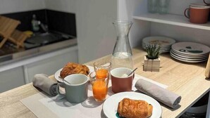 Esmorzar amb croissants, suc i una gerra damunt d'una taula de fusta a una cuina moderna amb armaris blancs i un sostre protegit.