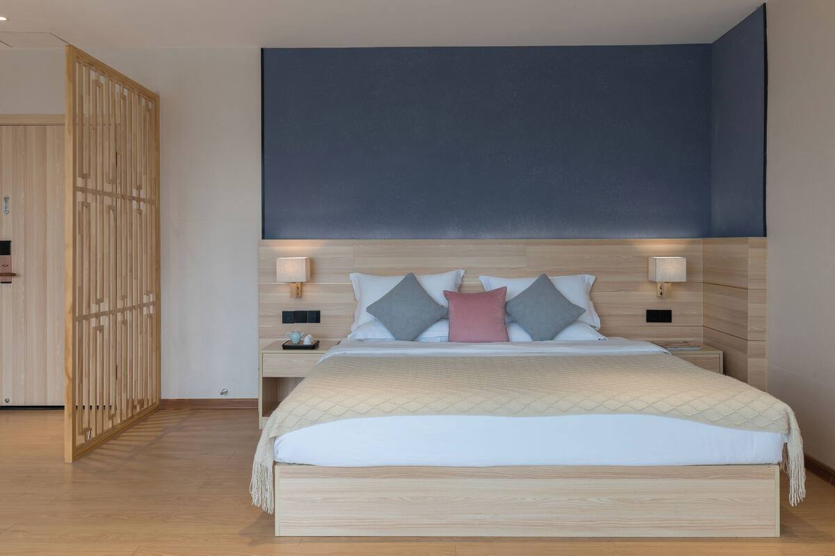 A modern bedroom with a large bed, wooden headboard, bedside lamps, and a wardrobe.