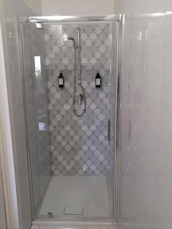 A glass-enclosed shower with a patterned wall, a handheld showerhead, and two wall-mounted controls. - Fondo Versace (Reggio Calabria)