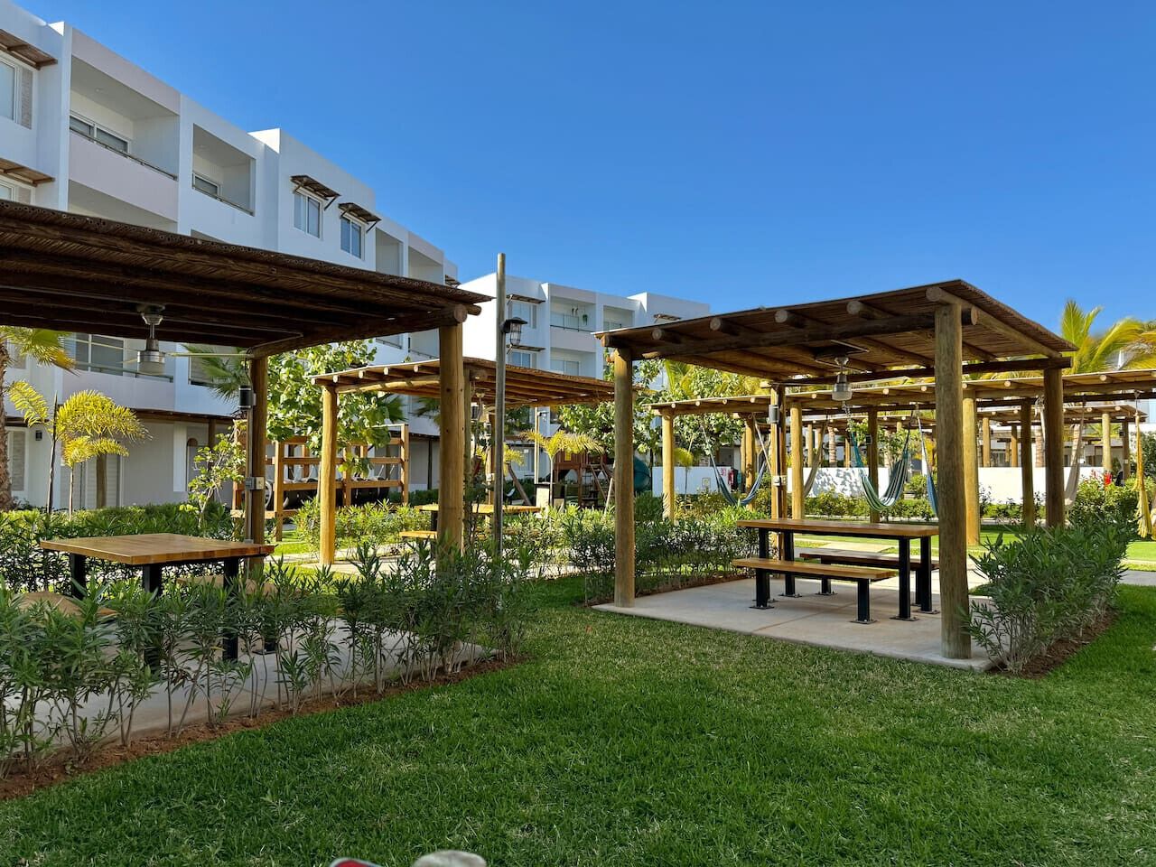 A courtyard with wooden pergolas, picnic tables, and a pool.