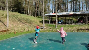 Two children playing on a green outdoor surface with a covered structure in the background.