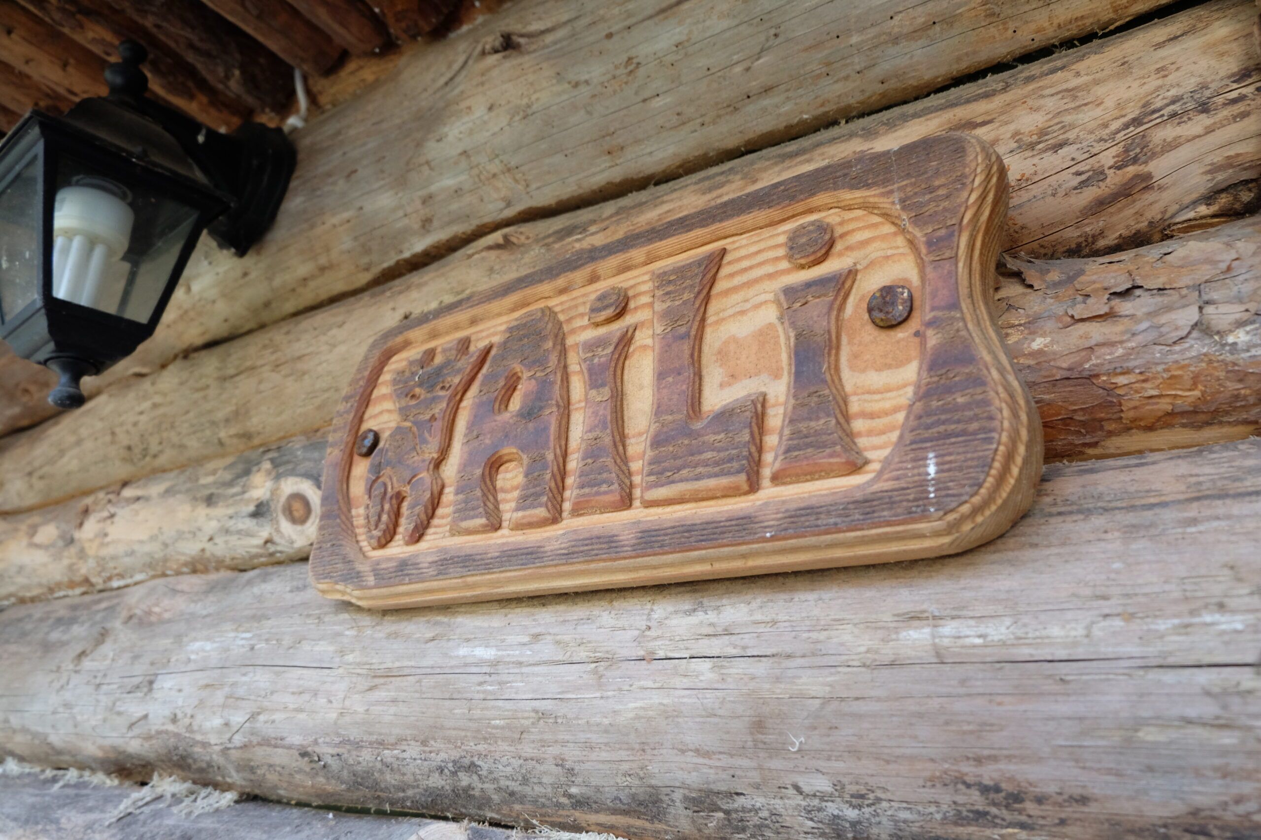 A wooden sign with the name "GAILI" carved into it, mounted on a log cabin wall.