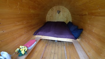 Un interior de madera con una cama, almohadas, una mesita con una toalla rosa y un ramo de flores.