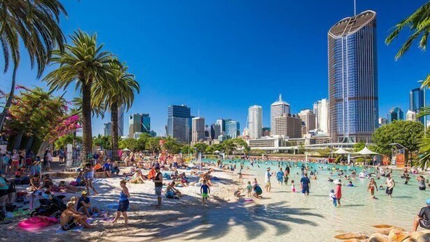 A beach with people, palm trees, and a city skyline in the background.
