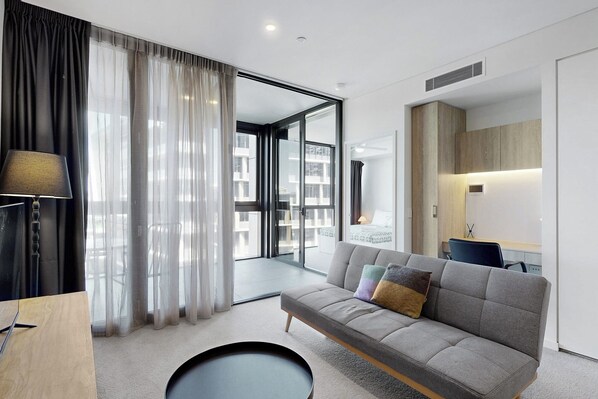 A modern living room with a grey sofa, a round coffee table, and a lamp. There is a sliding glass door leading to a balcony.