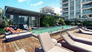 Zona de piscina en la azotea con sillones de descanso, piscina y edificio con cerramiento de vidrio que ofrece vistas del horizonte urbano.