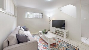 Un salon avec un canapé, une table basse, un téléviseur et un tapis à motifs.