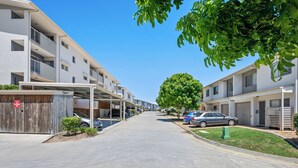 Una calle residencial con edificios de apartamentos modernos, estacionamiento techado y una acera bordeada de árboles.