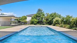 Una piscina rectangular con agua azul cristalina, rodeada por un borde de hormigón y una valla metálica.