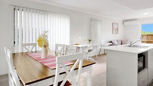 A modern kitchen with white cabinetry, a central island, and a dining area with a wooden table and white chairs.
