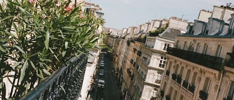A narrow urban street with buildings on either side, a metal railing on the left, and a clear sky above.
