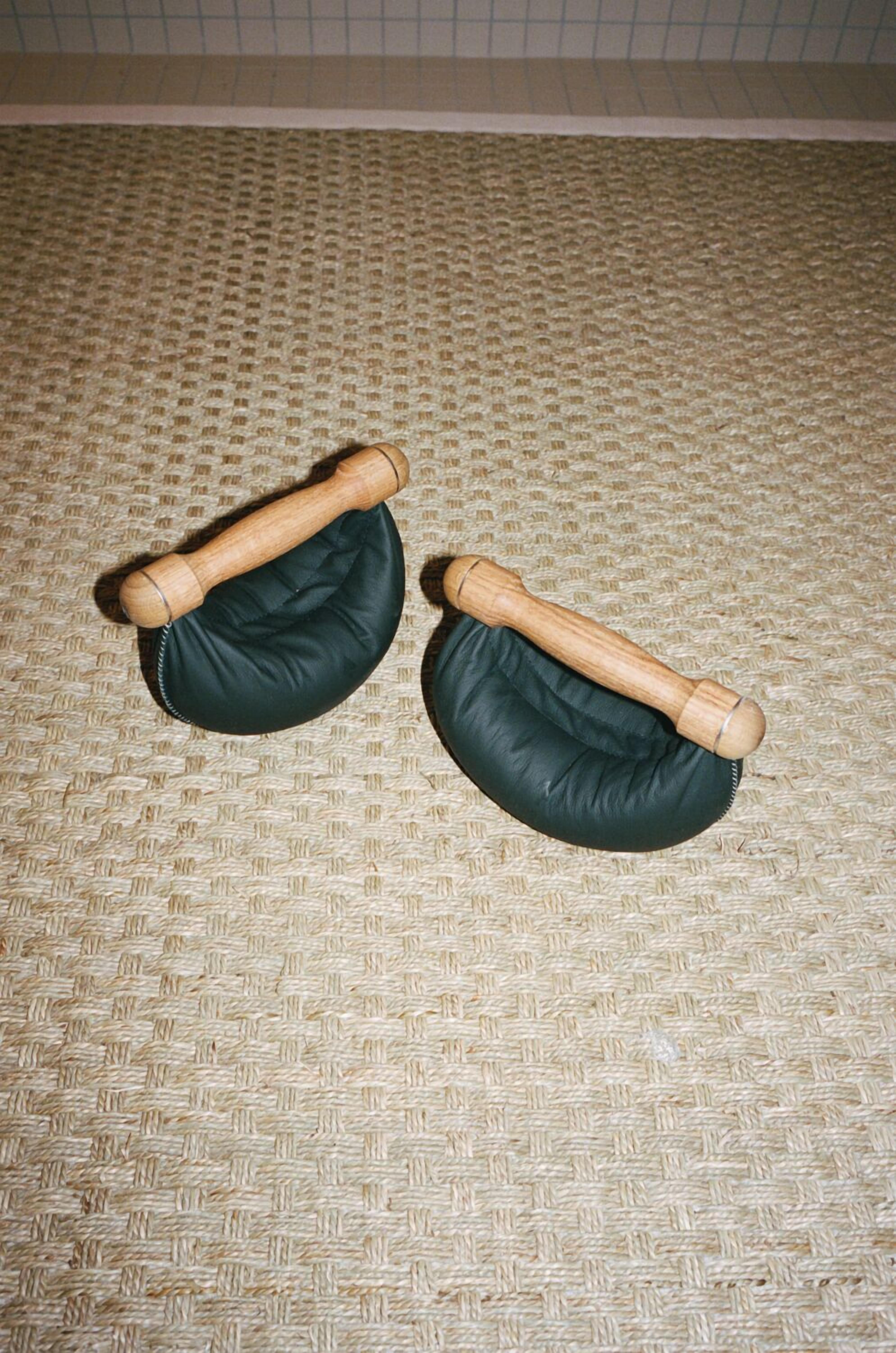 Dos pelotas de masaje negras con mangos de madera sobre un suelo tejido.