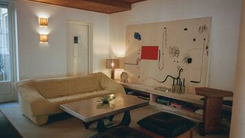 A living room with a beige sofa, a coffee table, a wooden side table, and a large abstract painting on the wall.