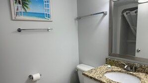 A bathroom with a toilet, sink, mirror, towel rack, and a painting of a beach scene.