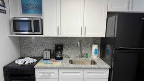 A kitchen with white cabinets, a microwave, a toaster, a coffee maker, a sink, and a refrigerator.