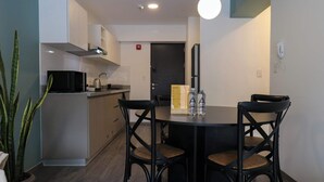 A modern kitchen with white cabinets, a black countertop, and a built-in microwave. There is a dining table with four chairs and a hanging light fixture above it. - w* | Warm 1BR in Historic Cusco w/ Balcony (Cusco)