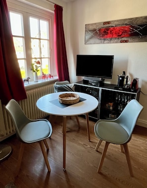A room with a round table, two chairs, a TV, and a radiator.