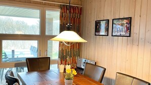 Un comedor con paneles de madera, una mesa grande, sillas, una lámpara colgante y dos carteles enmarcados en la pared.