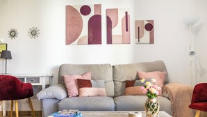 A living room with a grey sofa, red chairs, a coffee table with books and a vase, and abstract wall art.