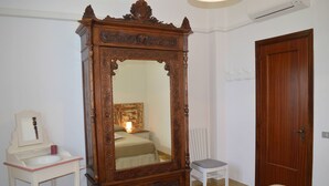 A bedroom with a large ornate wooden bed frame, a bedside table with a lamp, a small chair, and a wooden door. - Casa Ravello with Garden - My Rental Homes (Scala)