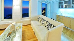 Una sala de estar acogedora con un sofá blanco, una mesita de centro y vistas al atardecer a través de amplias ventanas.