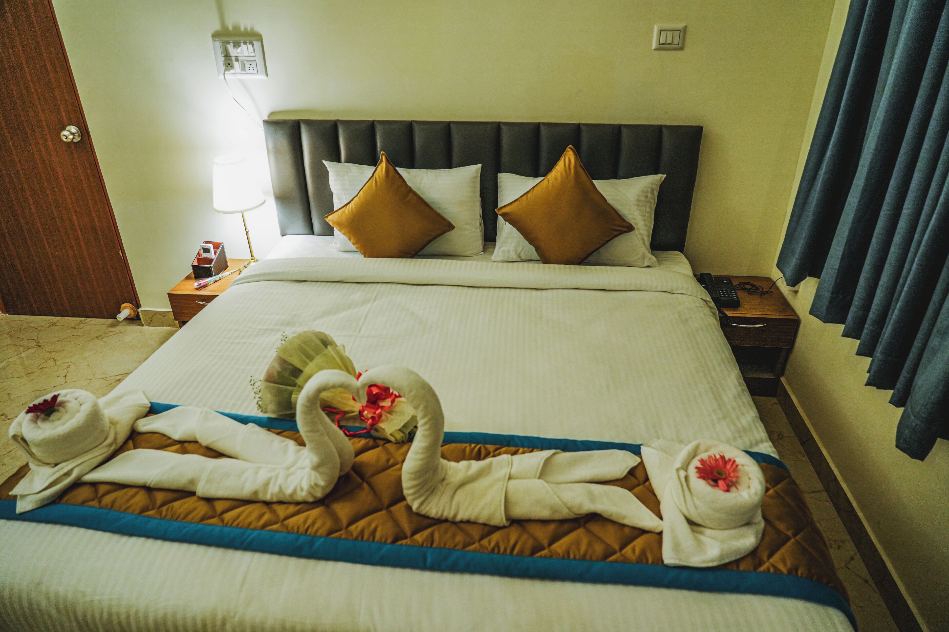 A hotel room with a large bed, two pillows, a bedside table with a lamp, and a nightstand with a phone.