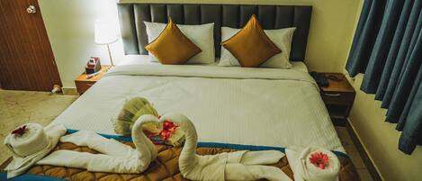 A hotel room with a large bed, two pillows, a bedside table with a lamp, and a nightstand with a phone.