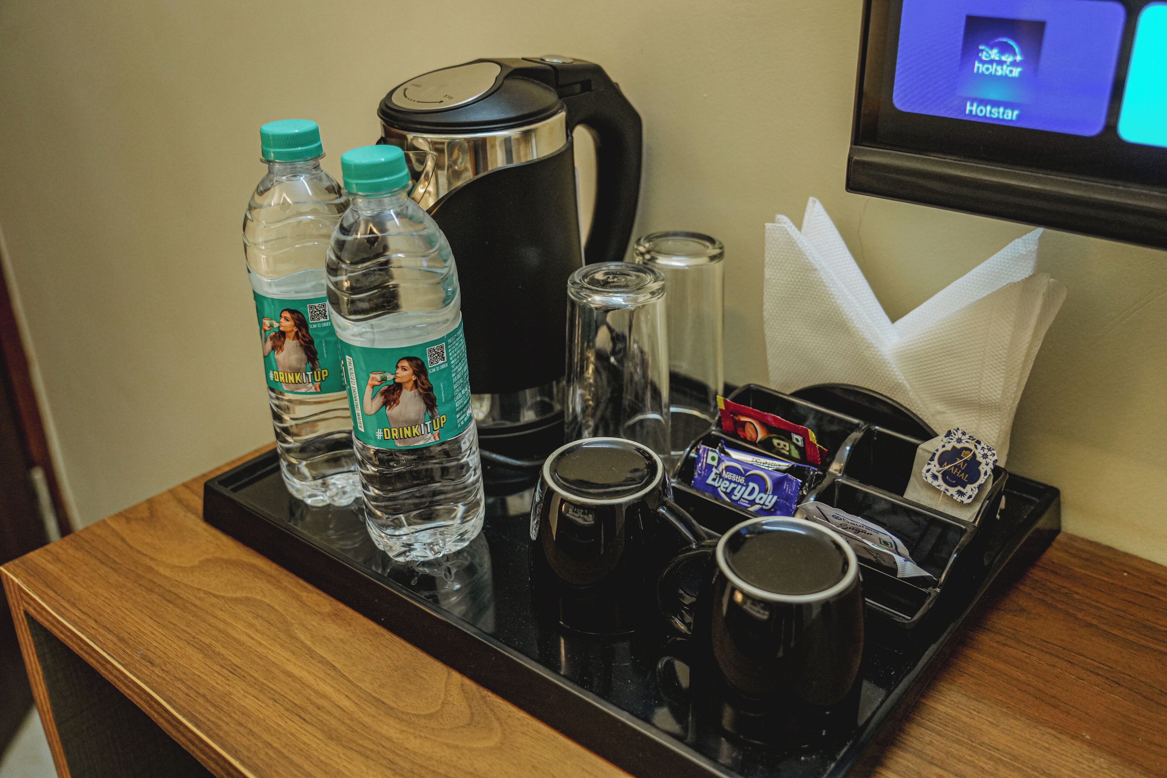 A tray with two water bottles, a coffee maker, a glass, a box of tissues, and a napkin holder.