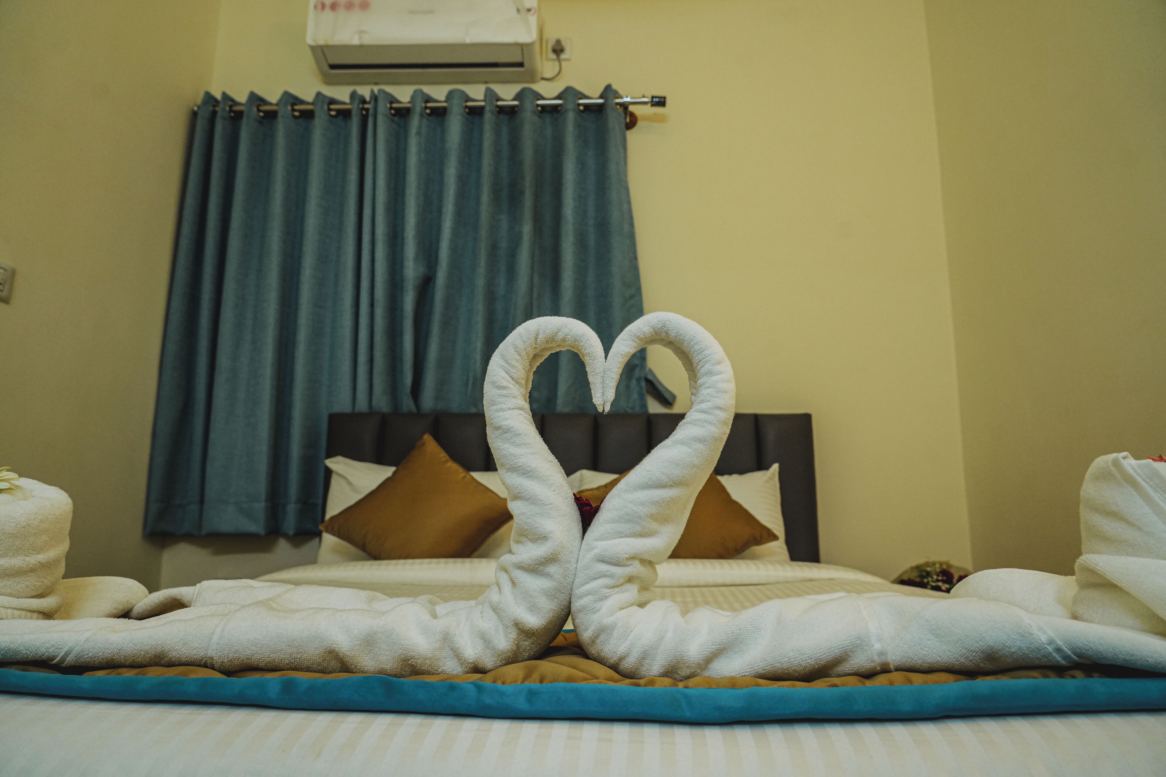 A hotel room with a bed, a blue curtain, and a heart-shaped towel arrangement.