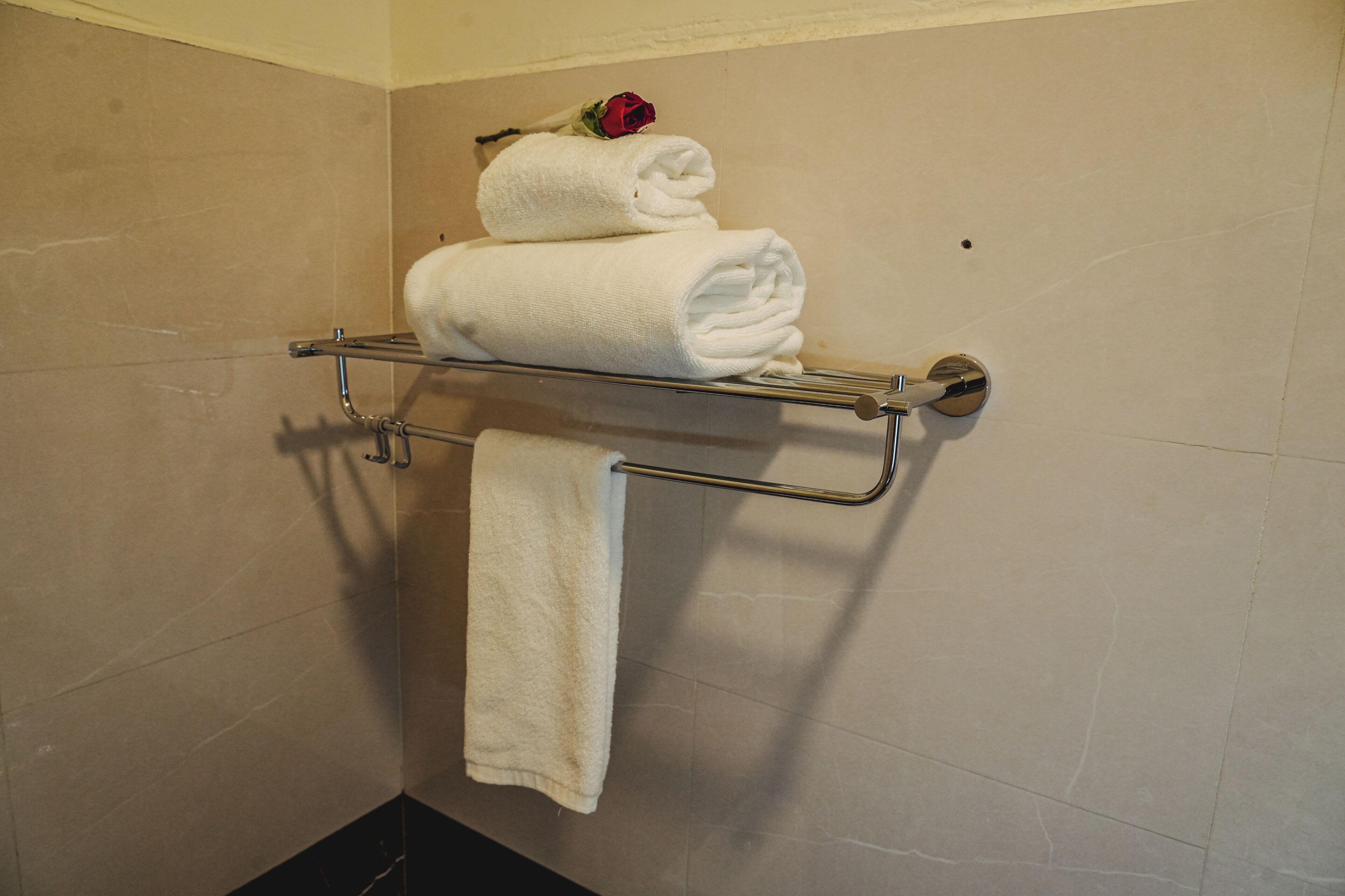 A bathroom with a towel rack holding folded towels and a rose.