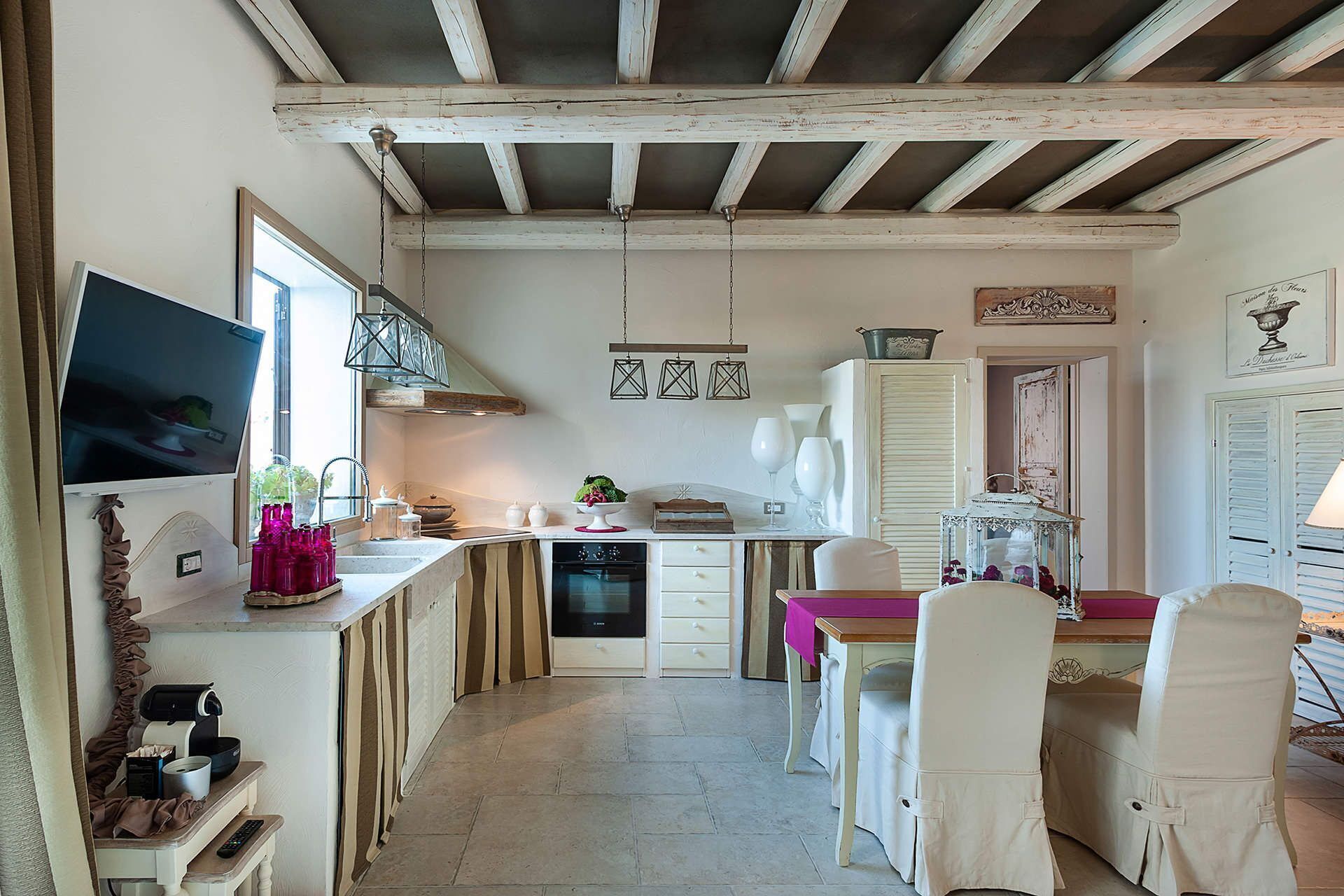 A compact kitchen with a dining area, featuring a TV, wooden beams, and a small dining table with chairs.