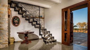 Una escalera moderna con barandilla metálica, una mesa redonda de madera con un florero y una puerta que da a un espacio exterior.