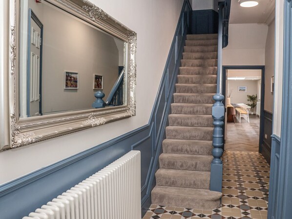 Eine Treppe mit blauer Handlauf, beigeem Teppich und einem weißen Heizkörper an der Wand.
