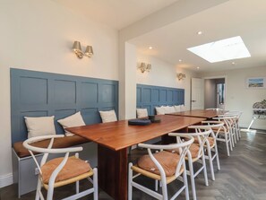 A dining area with a long wooden table, white chairs with brown cushions, and blue paneled walls. - Coral Villa (Bridlington)