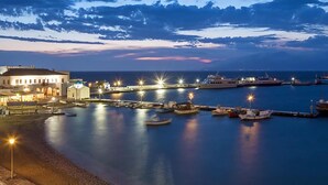 A coastal marina at dusk with boats docked, a pier, and buildings along the waterfront.