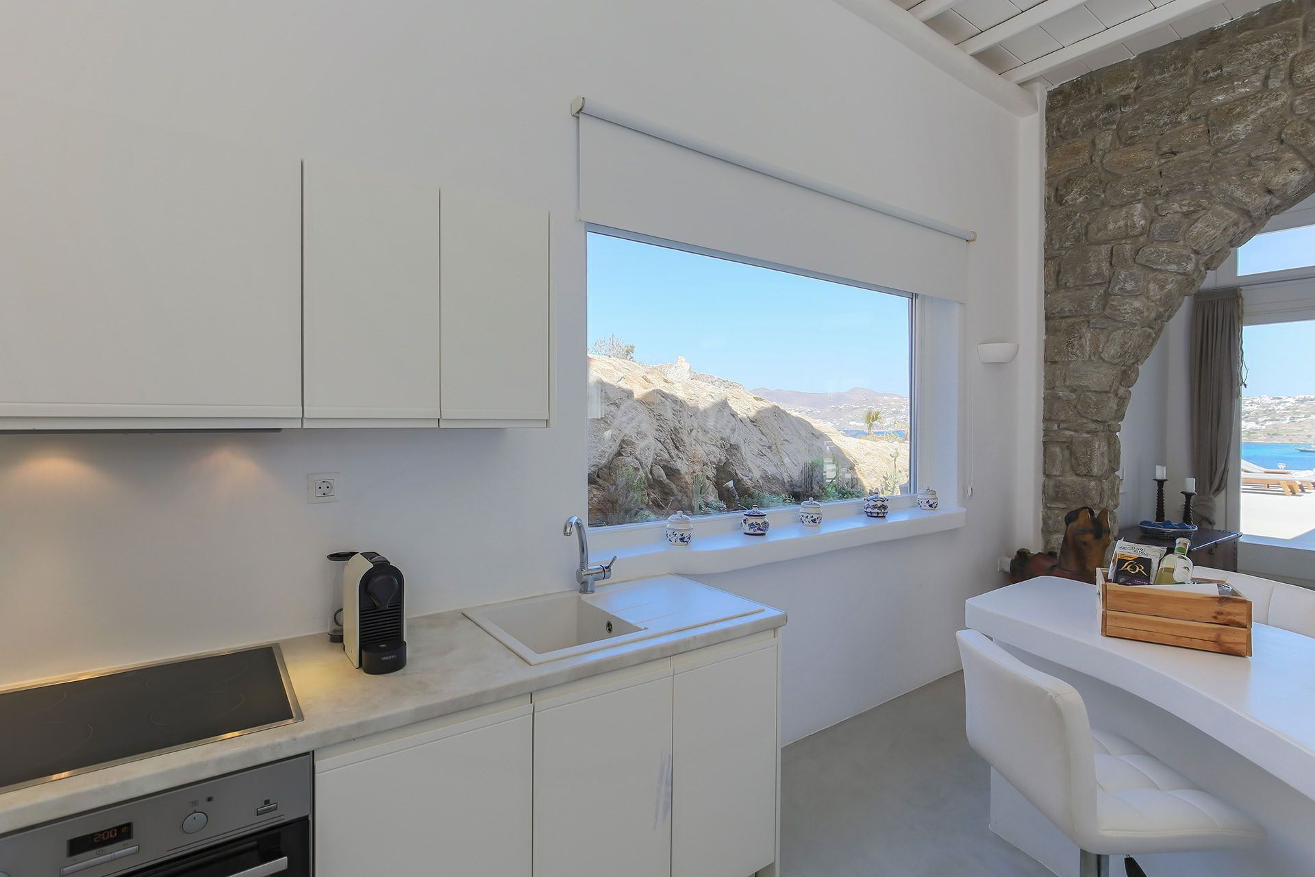 Una cocina moderna con armarios blancos, estufa integrada y ventana con vistas a un paisaje rocoso.
