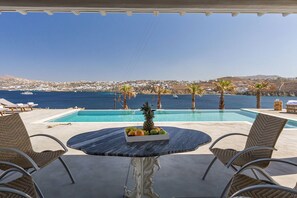 Ein Poolbereich mit Tisch, Stühlen und Blick auf das Meer und entfernte Gebäude.