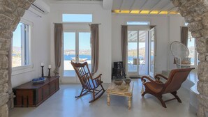 Une pièce spacieuse avec vue sur la mer, comprenant un fauteuil à bascule en bois, une petite table et un mur en pierre.