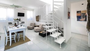 Un salon moderne avec un escalier blanc, un coin repas avec une table et des chaises, et un téléviseur fixé au mur.