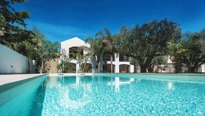 Piscina com água azul cristalina, rodeada por vegetação exuberante e um edifício branco com várias varandas.