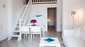 Ein zeitgemäßer Wohnraum mit einer weißen Wendeltreppe, einem Essbereich inklusive Tisch und Stühlen, einer Couch und einer Lampe.