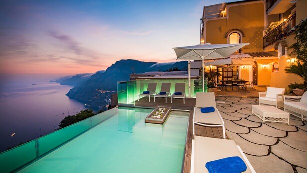 A rooftop infinity pool with lounge chairs and a table, overlooking a scenic coastline at sunset. - Villa Amanda with private pool - My Rental homes (Positano)
