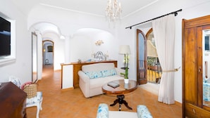 A spacious living room with a sofa, a round coffee table, and a chandelier. There is a wooden cabinet and a view of the outside balcony. - Villa Amanda with private pool - My Rental homes (Positano)