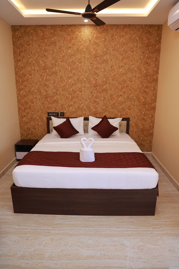 A neatly made bed with a brown headboard, a white blanket, and a decorative swan pillow. - JPD Residency (Thindukkal)