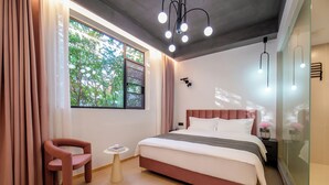 A modern bedroom with a large bed, a small side table, a chair, and a window with curtains. - Homie Inn (Changsha)