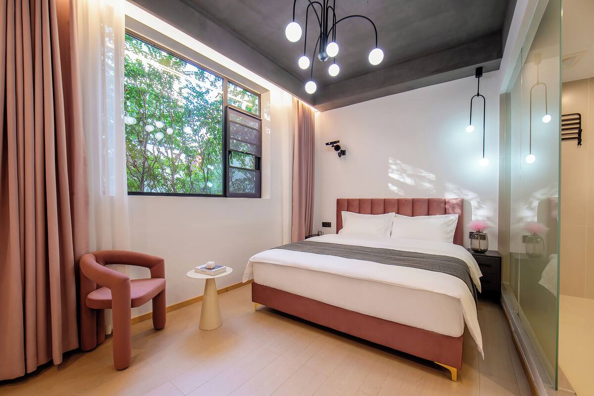 Une chambre à coucher moderne avec un grand lit, une petite table de chevet, une chaise et une fenêtre avec des rideaux.