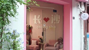 A hotel entrance with a pink exterior, a glass door, and two pink chairs outside. - Homie Inn (Changsha)