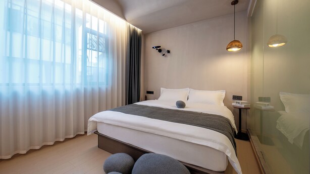 A modern hotel room with a large bed, a bedside table, a nightstand, and a large window with sheer curtains. - Homie Inn (Changsha)