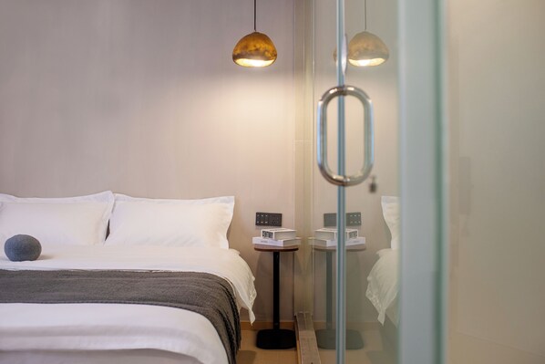 A modern hotel room with a neatly made bed, a small bedside table with a lamp, and a glass shower enclosure. - Homie Inn (Changsha)